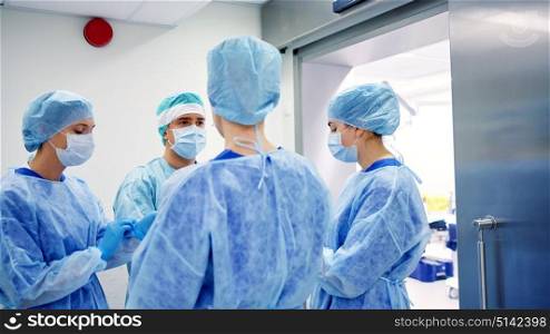 surgery, medicine and people concept - group of surgeons in operating room at hospital talking and preparing to operation. group of surgeons in operating room at hospital