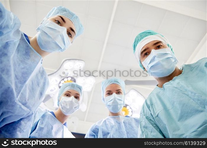 surgery, medicine and people concept - group of surgeons in operating room at hospital looking into camera