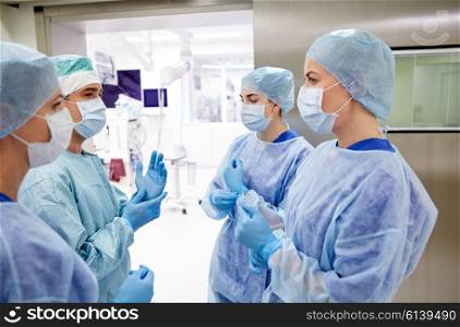 surgery, medicine and people concept - group of surgeons in operating room at hospital talking and preparing to operation