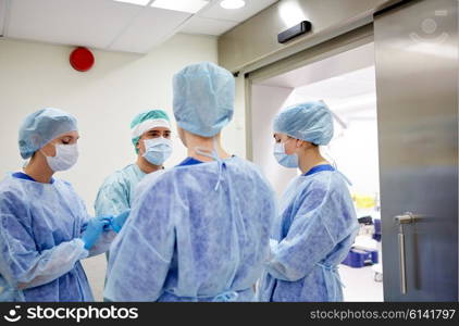 surgery, medicine and people concept - group of surgeons in operating room at hospital talking and preparing to operation