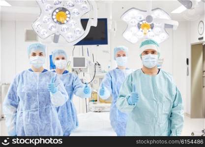 surgery, medicine and people concept - group of surgeons in operating room at hospital showing thumbs up