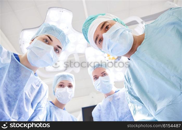 surgery, medicine and people concept - group of surgeons in operating room at hospital looking into camera