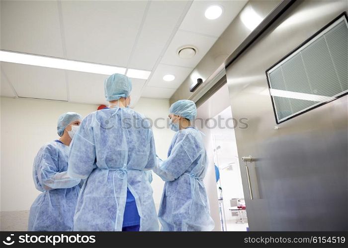 surgery, medicine and people concept - group of surgeons in operating room at hospital talking and preparing to operation