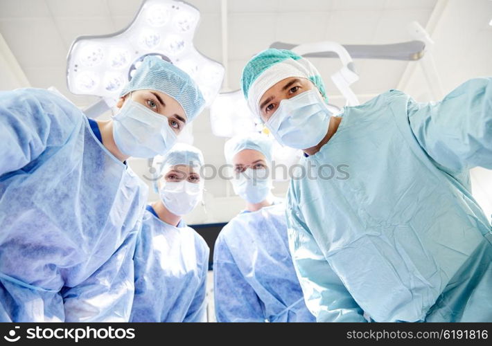 surgery, medicine and people concept - group of surgeons in operating room at hospital looking into camera