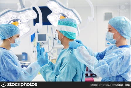 surgery, medicine and people concept - nurse assisting surgeon and helping with gloves and protective wear in operating room at hospital. surgeons in operating room at hospital