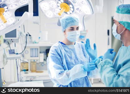 surgery, medicine and people concept - nurse assisting surgeon and helping with gloves in operating room at hospital. surgeons in operating room at hospital