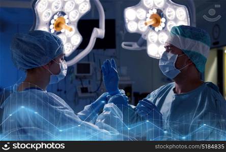 surgery, medicine and people concept - nurse assisting surgeon and helping with gloves in operating room at hospital. surgeons in operating room at hospital