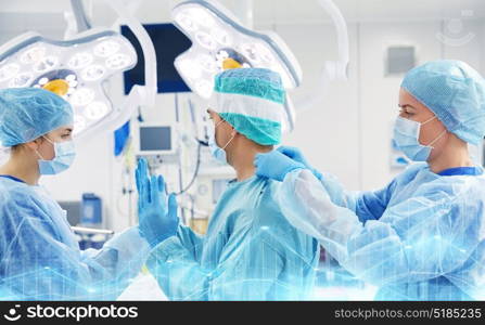 surgery, medicine and people concept - nurse assisting surgeon and helping with gloves and protective wear in operating room at hospital. surgeons in operating room at hospital