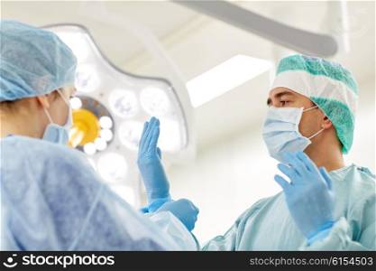 surgery, medicine and people concept - nurse assisting surgeon and helping with gloves in operating room at hospital
