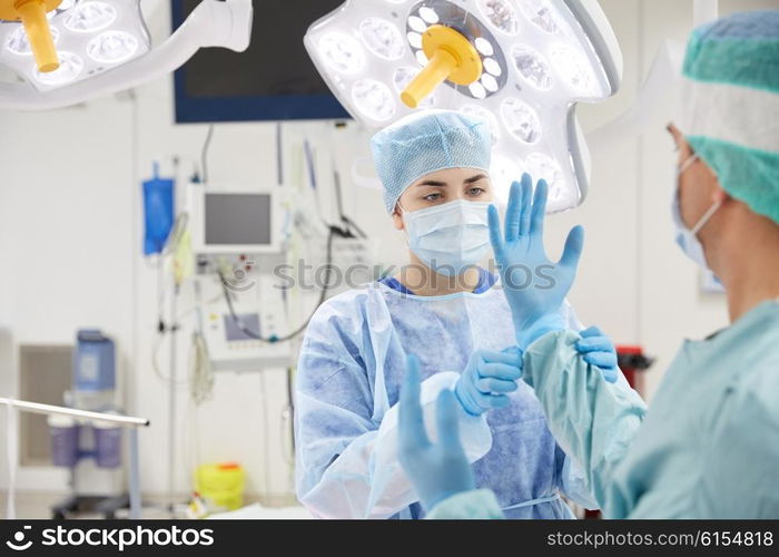 surgery, medicine and people concept - nurse assisting surgeon and helping with gloves in operating room at hospital