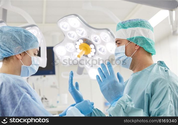 surgery, medicine and people concept - nurse assisting surgeon and helping with gloves in operating room at hospital