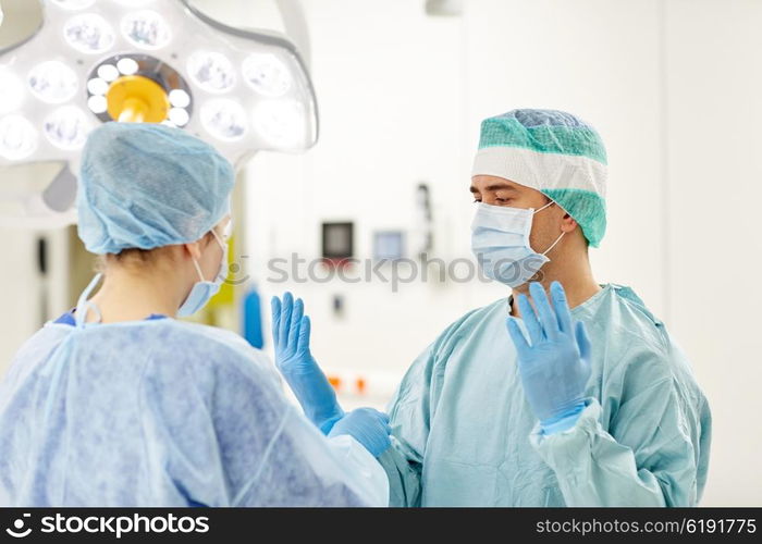 surgery, medicine and people concept - nurse assisting surgeon and helping with gloves in operating room at hospital