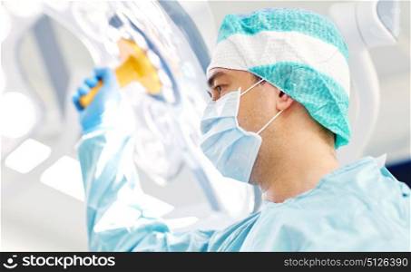 surgery, medicine and people concept - surgeon in mask adjusting lamp in operating room at hospital. surgeon in operating room at hospital