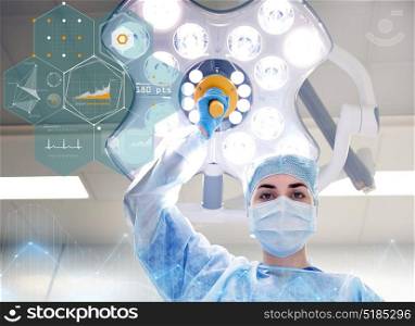 surgery, medicine and people concept - surgeon in mask adjusting lamp in operating room at hospital. surgeon in operating room at hospital