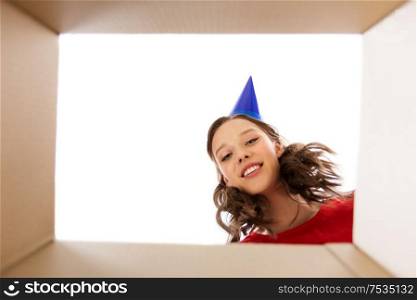 surprise, delivery and holiday concept - happy young woman in birthday party cap looking into open gift box. happy young woman looking into open birthday gift