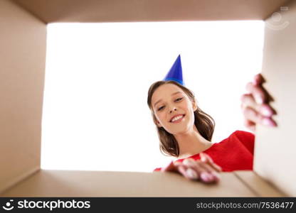 surprise, delivery and holiday concept - happy young woman in birthday party cap looking into open gift box. happy young woman looking into open birthday gift