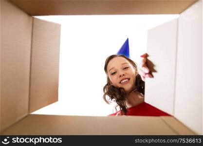 surprise, delivery and holiday concept - happy young woman in birthday party cap looking into open gift box. happy young woman looking into open birthday gift
