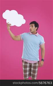 Surprise young man holding thought bubble over pink background