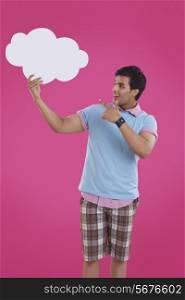 Surprise young man pointing at thought bubble over pink background