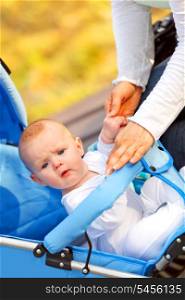Surprised baby girl sitting in stroller in park and holding mother&rsquo;s hand &#xA;