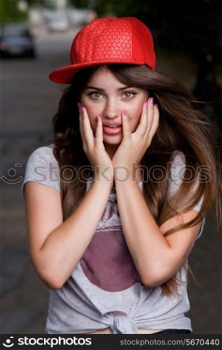 surprised beautiful emotional teen model on street. red cap, grey t-shirt, dark blue shorts