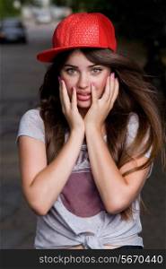 surprised beautiful emotional teen model on street. red cap, grey t-shirt, dark blue shorts