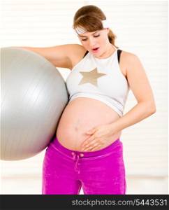 Surprised beautiful pregnant woman holding fitness ball and touching her belly at living room&#xA;