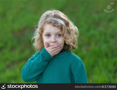 Surprised blond child with blue eyes covering his mouth