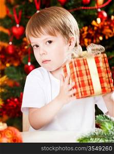 Surprised boy holding gift against Christmas tree with decorations