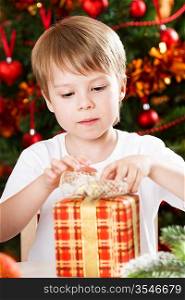 Surprised boy opening present against Christmas tree with decorations
