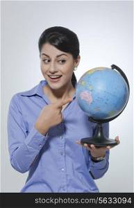 Surprised businesswoman pointing at globe against gray background