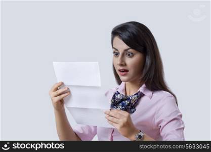 Surprised businesswoman reading document over gray background