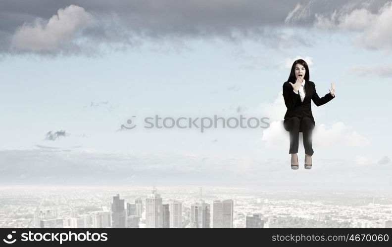 Surprised businesswoman. Young emotional businesswoman sitting on cloud above city