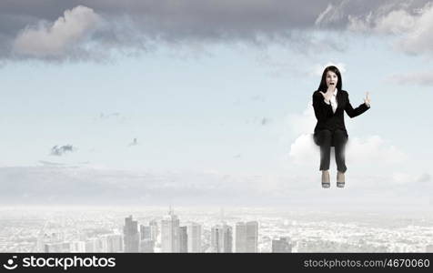 Surprised businesswoman. Young emotional businesswoman sitting on cloud above city