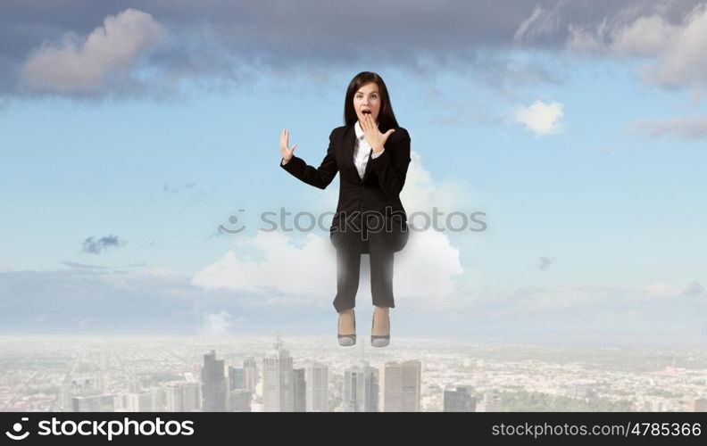 Surprised businesswoman. Young emotional businesswoman sitting on cloud above city