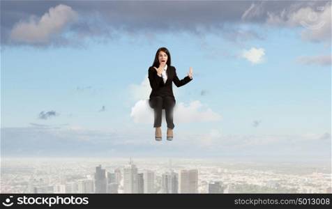 Surprised businesswoman. Young emotional businesswoman sitting on cloud above city