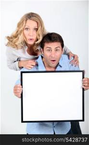 Surprised couple holding blank message board