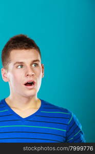 Surprised embarrassed male face, young man looking with shocked face expression on blue background