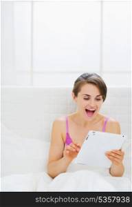 Surprised girl sitting in bed and using tablet PC