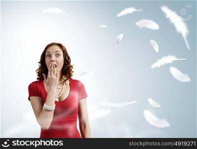 Surprised girl. Young pretty girl in red dress and feathers flying in air