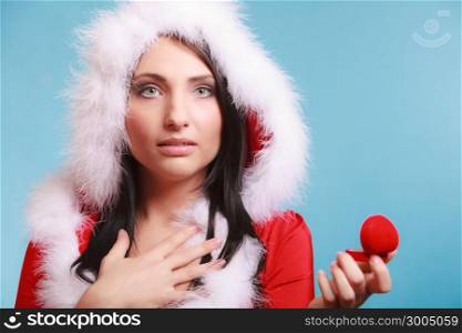 Surprised happy girl young woman wearing santa claus costume opening present red heart shaped gift box with engagement ring on blue background. Christmas time gifts.