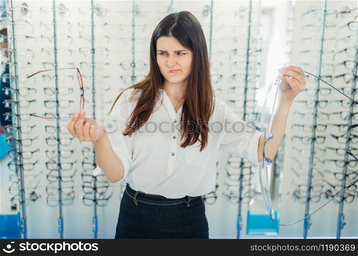 Surprised lady holds huge decorative glasses, optic store, showcase with spectacles on background. Professional eye care, eyeglasses choice. Surprised lady holds huge glasses in optic store