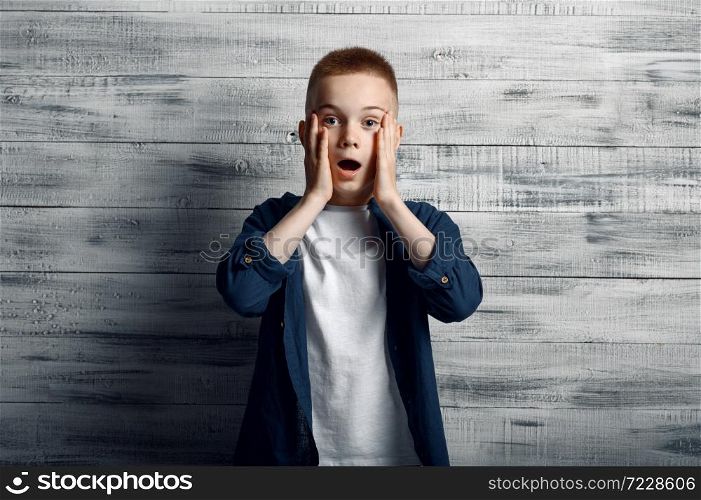 Surprised little boy in studio. Children and gadgets, kid isolated on wooden background, child emotion, schoolboy photo session. Surprised little boy in studio, wooden background