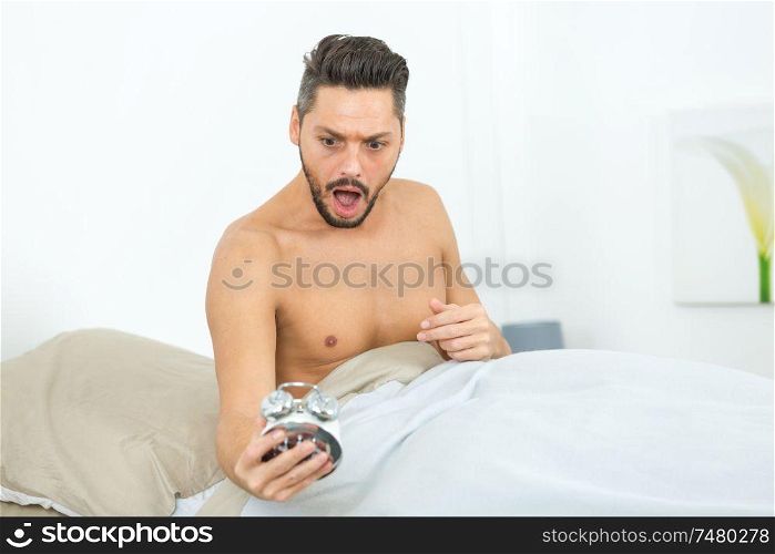 surprised man with alarm clock in bedroom