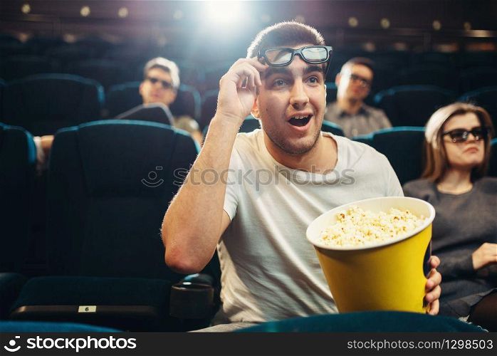 Surprised man with popcorn watching film in cinema. Movie entertainment