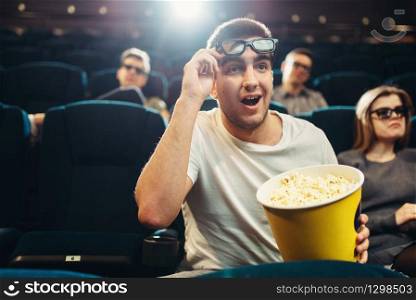 Surprised man with popcorn watching film in cinema. Movie entertainment