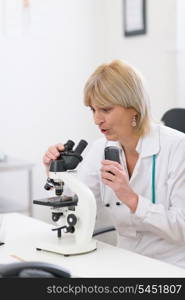 Surprised middle age doctor woman looking in microscope and making voice notes