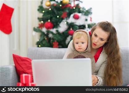 Surprised mother and baby near Christmas tree looking in laptop