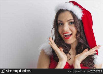 Surprised Santa girl. Christmas woman. Beauty model girl in Santa Hat. Funny Surprised Woman Portrait. Open Mouth. True Emotions. Red Lips and Manicure. Beautiful Holiday Makeup