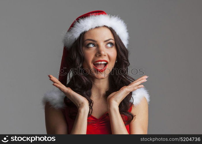 Surprised Santa girl. Christmas woman. Beauty model girl in Santa Hat. Funny Surprised Woman Portrait. Open Mouth. True Emotions. Red Lips and Manicure. Beautiful Holiday Makeup